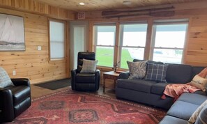 Relax in a spacious room with a large window offering a view of the surrounding green landscape, a comfortable seating area, and a patterned rug.