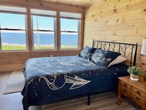 Relax in this serene bedroom with a large bed, a window offering a view of the sea and surrounding landscape.