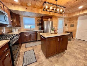 Enjoy cooking in this well-equipped kitchen with a central island, stainless steel appliances, and a wooden ceiling.