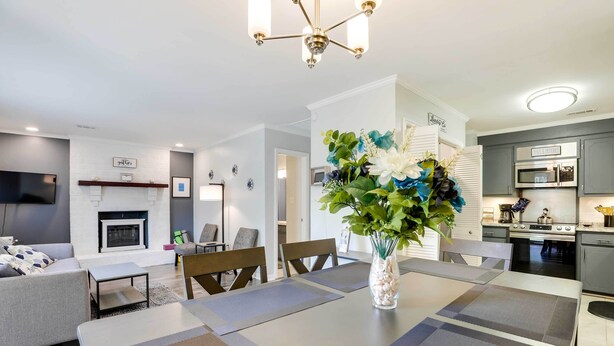 A modern living room with a fireplace, a dining area with a vase of flowers, and a kitchen with grey cabinets and stainless steel appliances. - North Charleston Vacation Rental Near Cooper River (North Charleston)