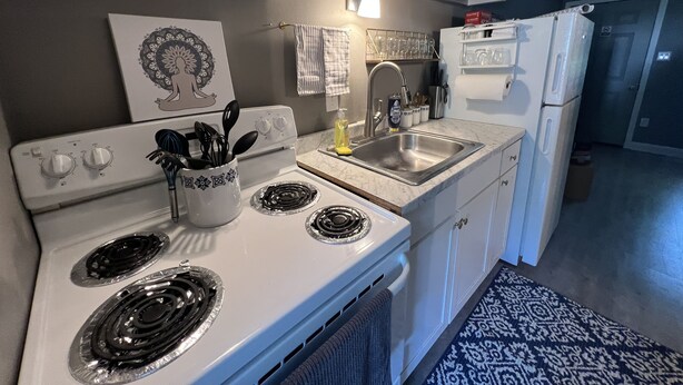 Una cocina con armarios blancos, estufa, pileta y refrigerador.