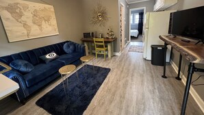 Un espacio habitable compacto con un sofá azul, una pequeña mesa de comedor, un televisor y un mapa mundial en la pared.