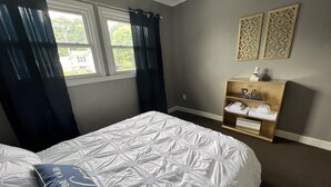 Un dormitorio ordenado con una cama grande, una mesita de noche con toallas y una ventana con cortinas.