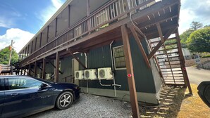 Un edificio con un espacio al aire libre cubierto, un coche aparcado cerca y suelo de grava.