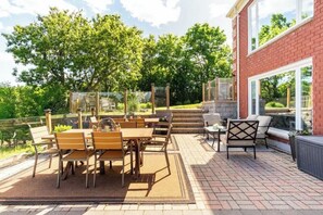 An outdoor patio with a brick floor, wooden furniture, and a view of a brick building.
