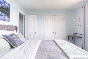 A bedroom with a bed, two white doors, a small table, and a wall-mounted anchor decoration.