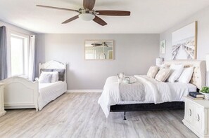 Un dormitorio con cama, mesita de noche, ventilador de techo y ventana con cortinas.