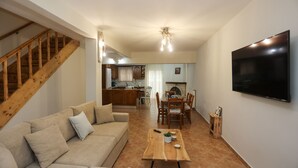Una sala de estar con una escalera de madera, un sofá, una mesa de centro de madera y un televisor fijado a la pared.