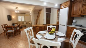Un comedor con mesa y sillas de madera, una cocina con armarios de madera y una sala de estar con sofá y televisor.