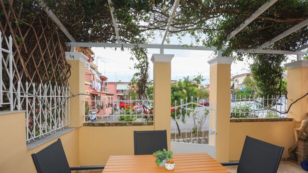 Un patio techado con una mesa de madera y sillas negras, una planta en maceta y vistas a la calle.