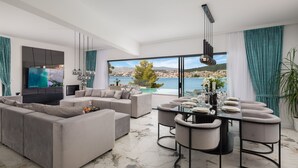 A modern living room with a large sofa set, a dining table with chairs, and a TV mounted on the wall. - Beachfront Villa Milka with Pool (Okrug Gornji)