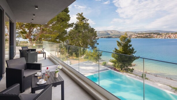 A balcony with a glass railing overlooking a pool and a scenic view of a lake and distant town. - Beachfront Villa Milka with Pool (Okrug Gornji)