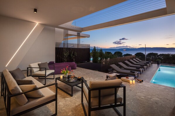 A modern outdoor lounge area with seating and a pool, overlooking a scenic view.