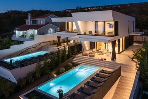 A modern two-story house with a swimming pool, outdoor seating, and a large patio area.