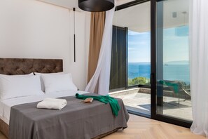 A bedroom with a bed, a view of the sea, and a balcony with a chair.