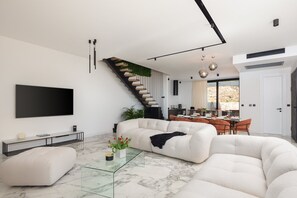 A modern living room with a large sectional sofa, a glass coffee table, and a flat-screen TV mounted on the wall.