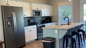 A modern kitchen with white cabinets, stainless steel appliances, a granite countertop, and black bar stools. - Lake Escape at Station 46 (Gravois Mills)
