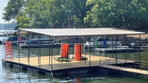 A dock with a covered seating area, a lifebuoy, and a boat in the background. - Lake Escape at Station 46 (Gravois Mills)