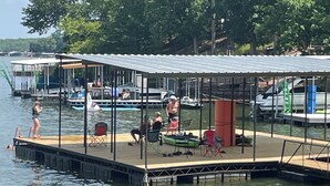 A docked boat with a covered area, a swimming area, and a dock extending into the water. - Waters Edge at Station 46 (Gravois Mills)