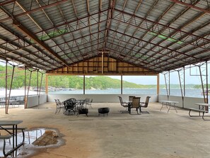Un espace extérieur abrité, doté de tables et de chaises, qui offre une vue sur un plan d’eau et sur la végétation environnante.