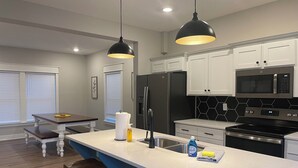 A modern kitchen with white cabinets, a large island with stools, stainless steel appliances, and pendant lighting. - Waters Edge at Station 46 (Gravois Mills)