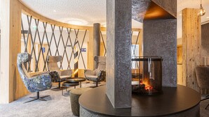 Un espace de détente moderne avec une cheminée centrale, des sièges confortables et un mur de séparation en bois.