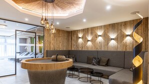 Un espace de détente moderne avec un mur d’accent en bois, une table ronde en bois et un luminaire noir aux lignes courbes.