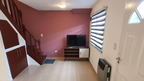 A living room with a TV, a small cabinet, a radiator, and a door. - Apartamento Hermoso y muy Cómodo (Ushuaia)
