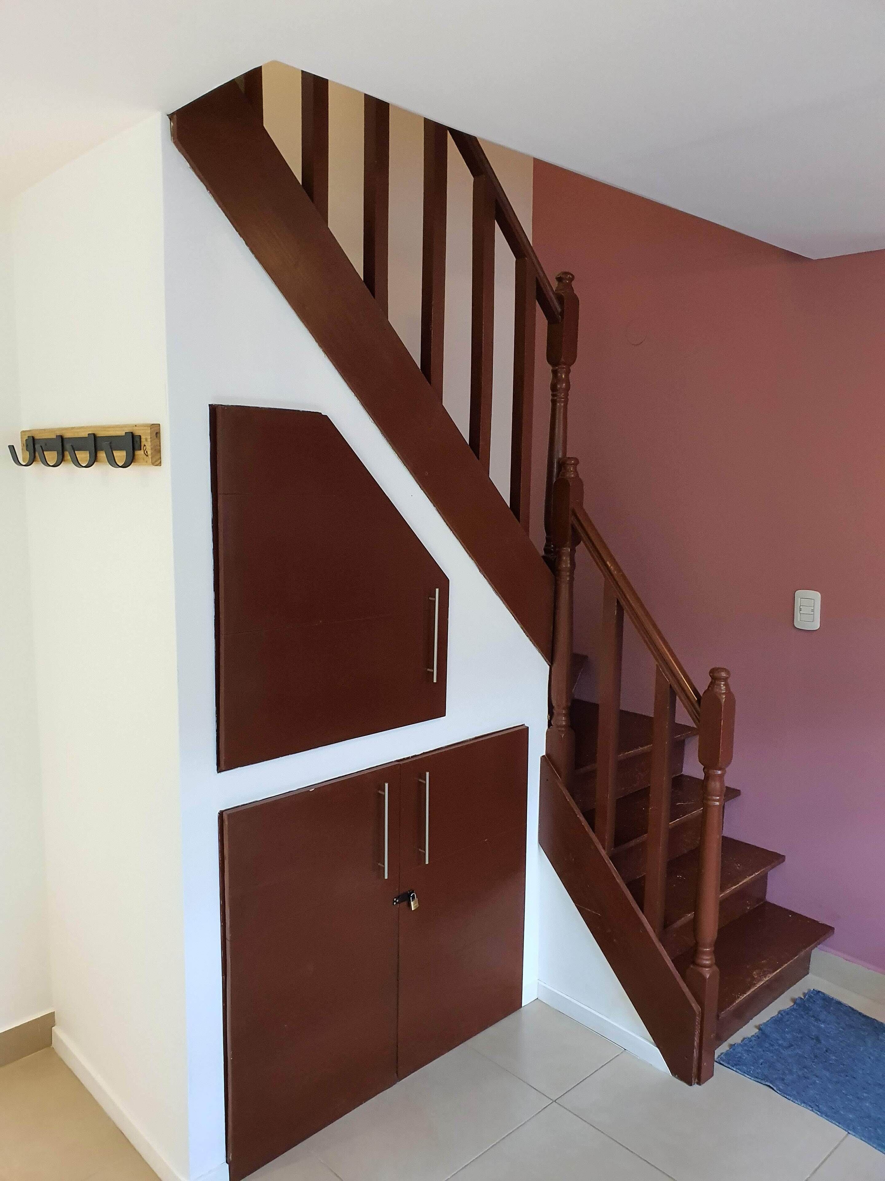 Un escalier avec des marches en bois et une rampe, menant à un palier où se trouvent un porte-manteau et un meuble.