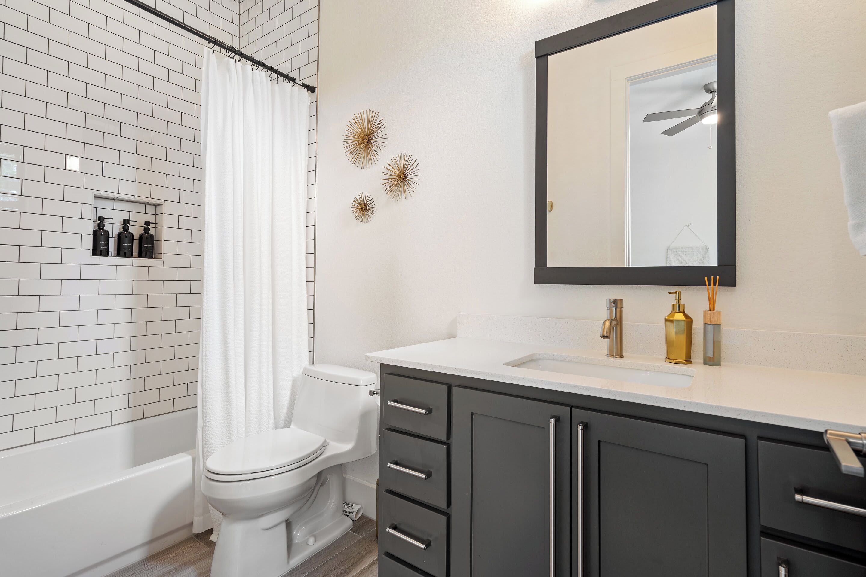 A modern bathroom with a white tiled shower, a toilet, a vanity with a mirror, and a bathtub.
