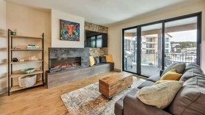 Una sala de estar moderna con chimenea, un sofá, una mesa de centro y un ventanal con vistas a edificios.