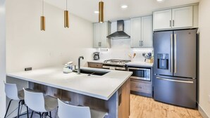 Una cocina moderna con una isla central, electrodomésticos de acero inoxidable e iluminación colgante.