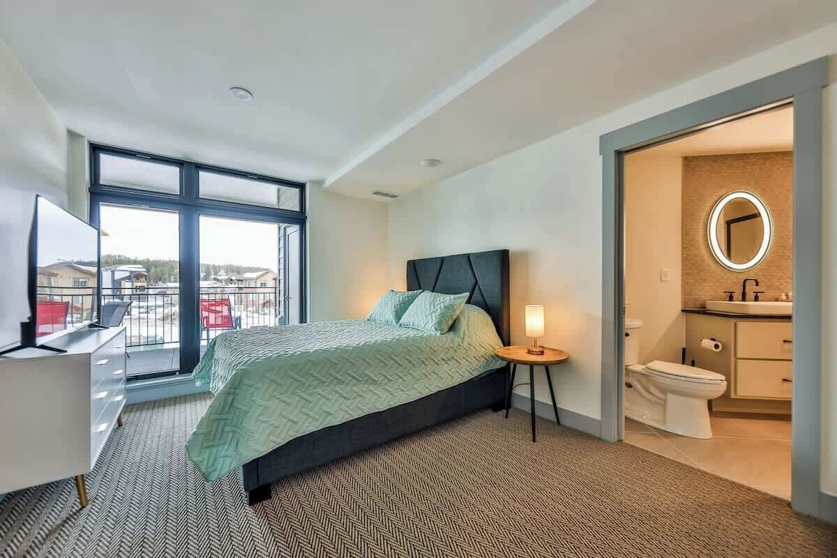 Una habitación de hotel moderna con una cama grande, un escritorio y un baño con espejo y lavamanos.