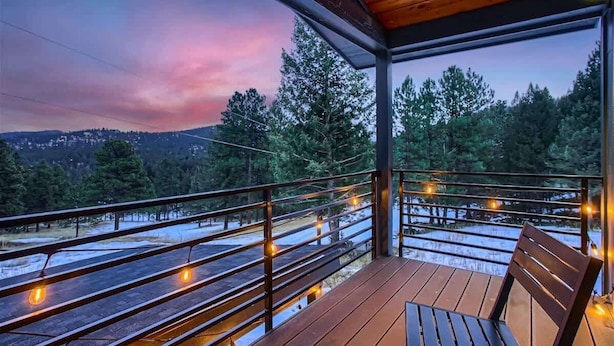 A wooden deck with a bench, overlooking a snowy landscape and trees.