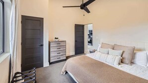 A bedroom with a bed, a dresser, a ceiling fan, and a door.