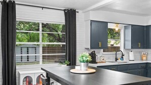 A modern kitchen with dark cabinets, a central island, and a window with curtains. - The Oak on 6th Walk to the Historic Square (Georgetown)