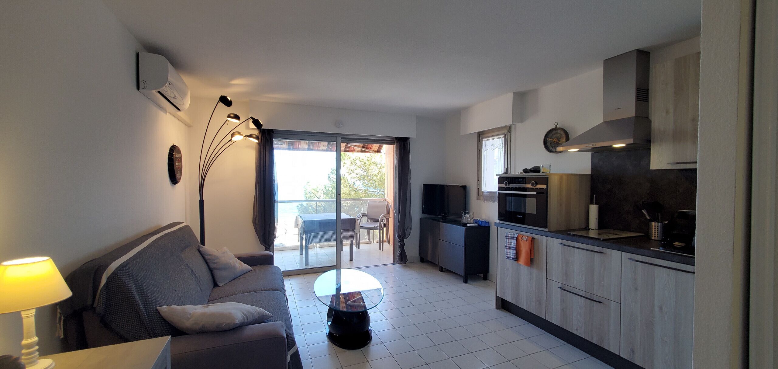 Een moderne woonkamer met een bank, salontafel en televisie. Grenzend daar aan een keuken met kookplaat, oven en magnetron.