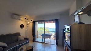 Ein Wohnzimmer mit Sofa, Couchtisch, TV-Schrank und Meerblick durch eine Glasschiebetür.