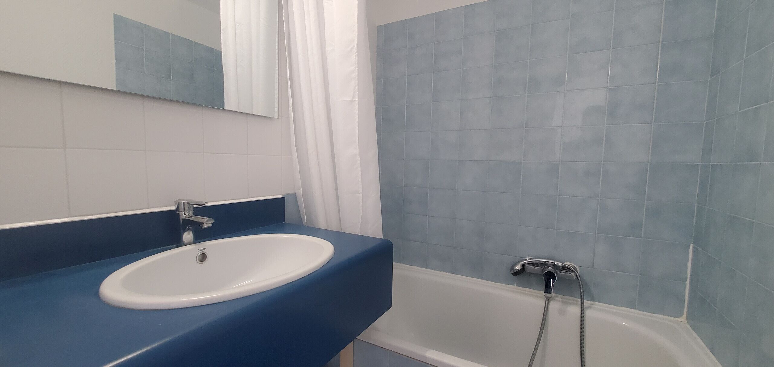 A bathroom with a white sink, blue countertop, and a bathtub with a showerhead.
