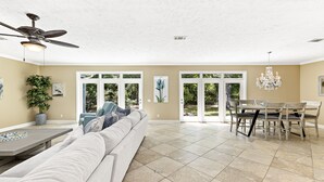 A spacious living area with a large sofa, dining table, and chairs. There is a ceiling fan, a chandelier, and a potted plant. - 4br House-Backyard -Pet-friendly-Bay Acess -W-fi (Gulf Shores)