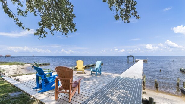 A wooden deck with Adirondack chairs overlooking a calm body of water. - 4br House-Backyard -Pet-friendly-Bay Acess -W-fi (Gulf Shores)