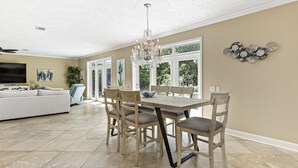 A spacious living room with a beige sofa, a dining table with chairs, and a chandelier. - 4br House-Backyard -Pet-friendly-Bay Acess -W-fi (Gulf Shores)