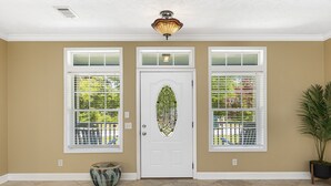 A beige-walled entryway with a white door, two windows with white blinds, and a potted plant. - 4br House-Backyard -Pet-friendly-Bay Acess -W-fi (Gulf Shores)