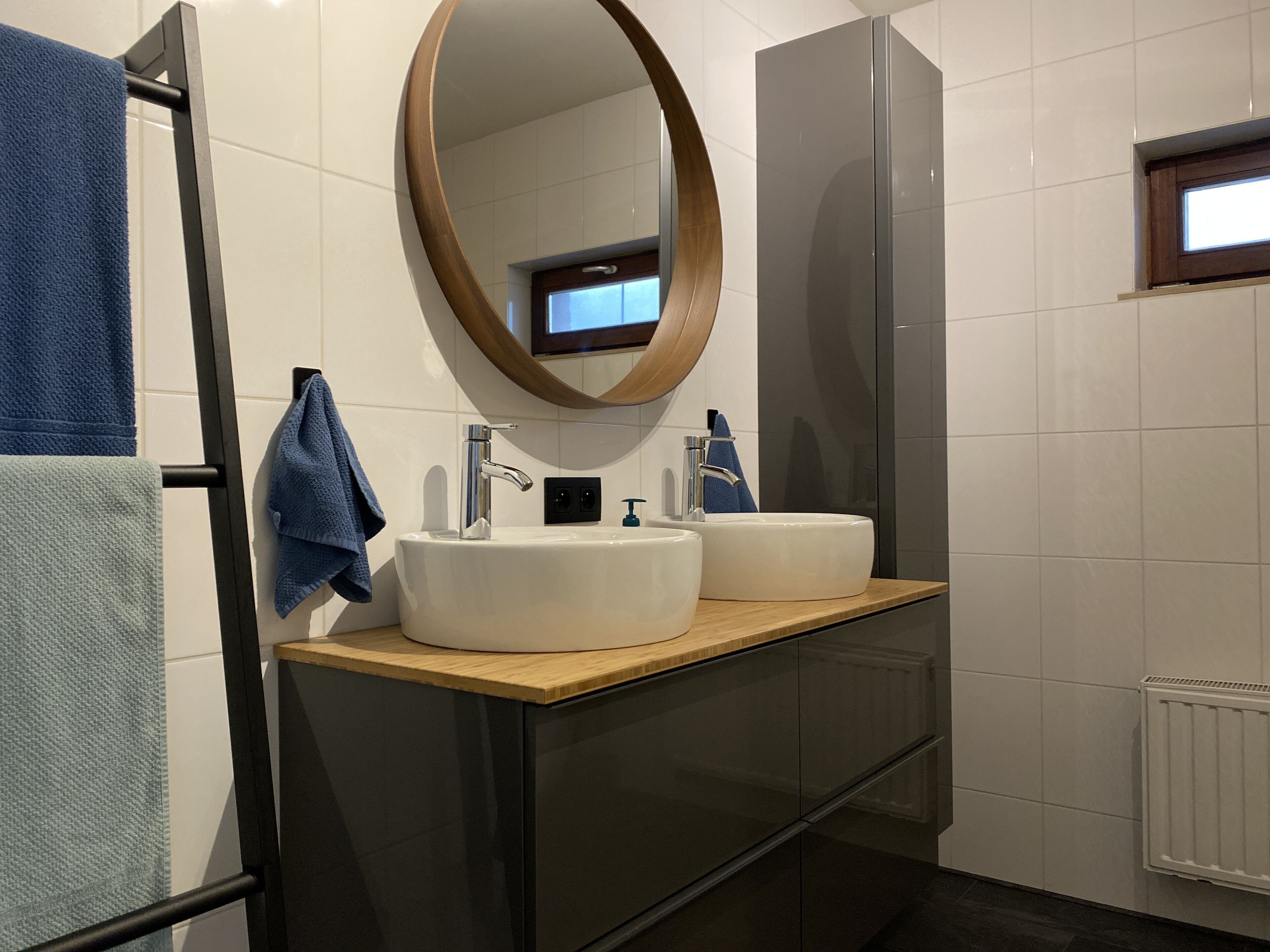 A modern bathroom with a wooden vanity, two sinks, a mirror, and a towel rack.