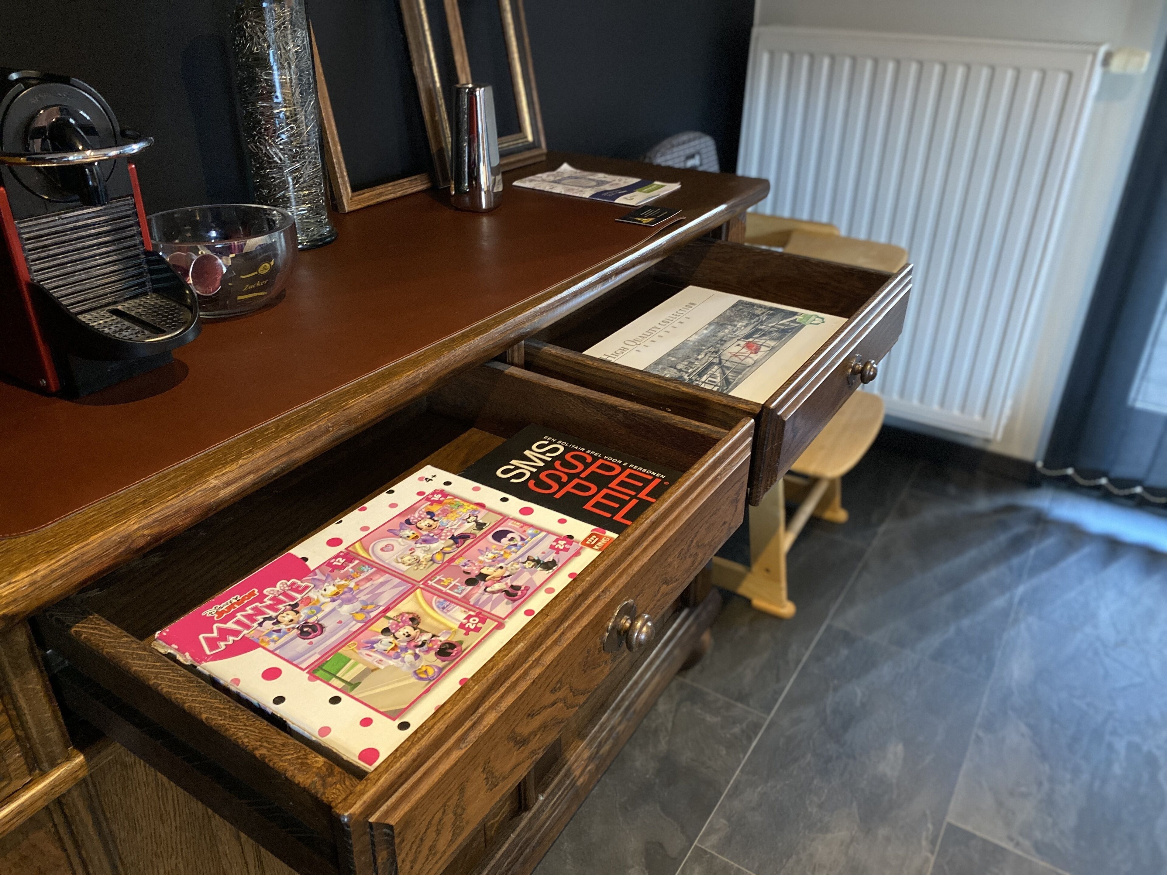 Un escritorio de madera con un cajón que contiene un libro con tema de 'Minions' y un libro 'SMS SPELSEL'.