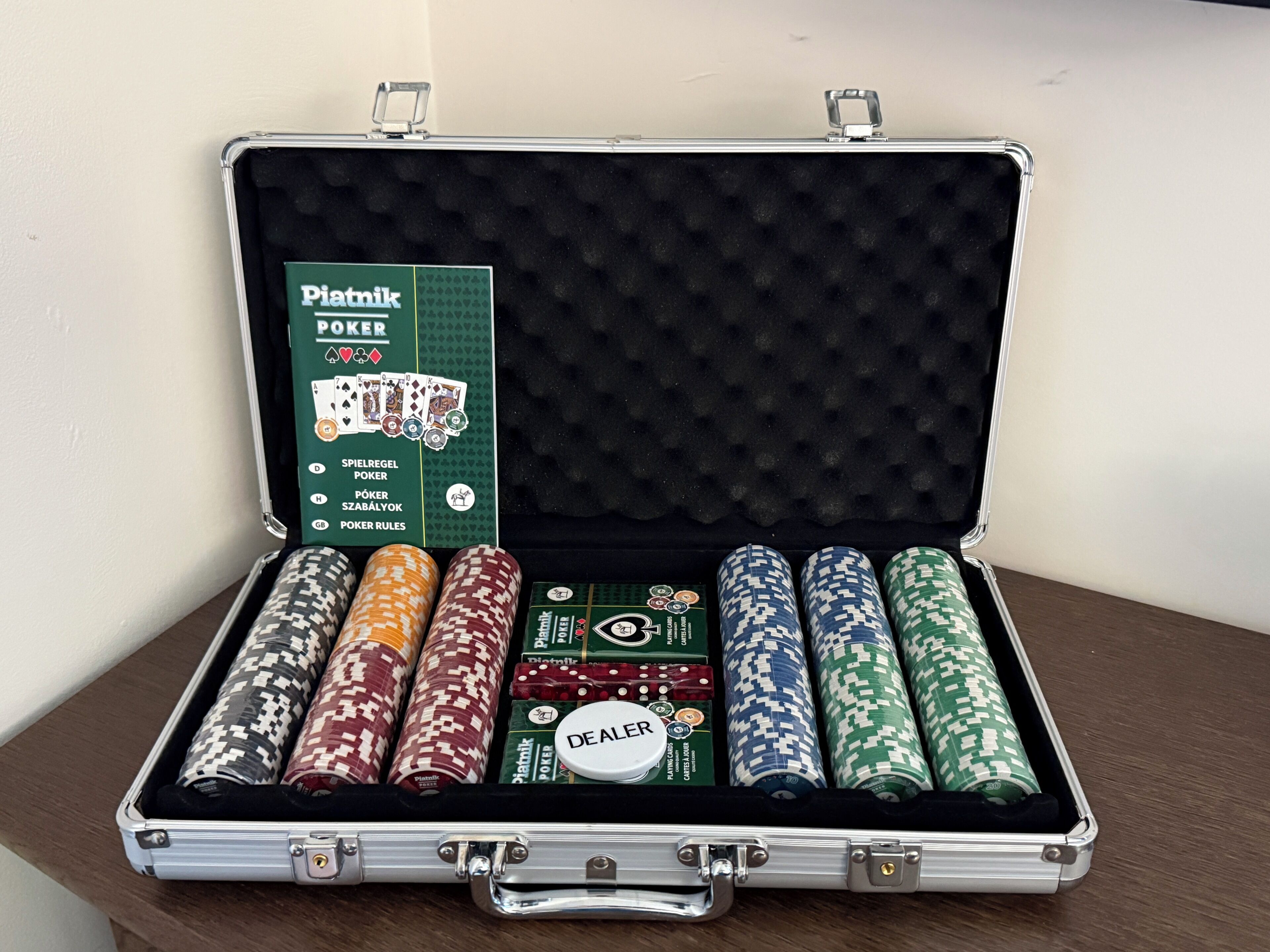 Ett pokerset i ett fodral med en grön etikett, pokermarker i olika färger och en markörbricka för den som delar ut korten.
