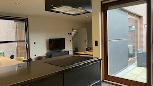 Moderni keittiö, jossa on sisäänrakennettu liesi, ruokailutila tuoleineen sekä suuri liukuovi, joka johtaa terassille.