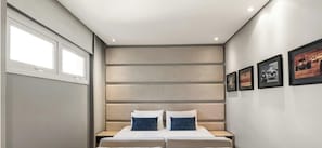 Une chambre à coucher avec un lit, une tête de lit, une fenêtre et des tableaux encadrés accrochés au mur.