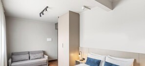 Habitación de hotel con cama, mesita de noche, lámpara, sofá e iluminación en el techo.