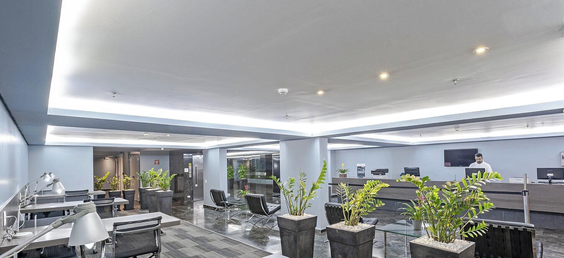 A modern hotel lobby with a reception desk, seating area, and potted plants.